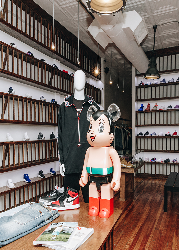 Streetwear store interior with sneakers, mannequin in black hoodie, and Astro Boy figure on display table.