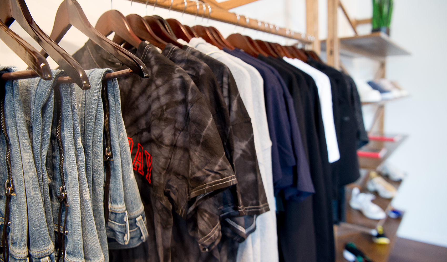 Assorted men's streetwear tops and denim jackets on wooden hangers in a modern store
