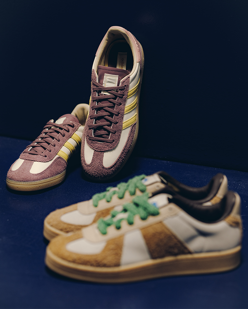 Two pairs of suede low-top sneakers, one with purple and yellow accents, the other with beige and green details, displayed on a dark surface.