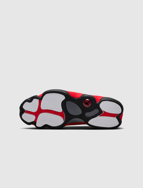 Red and black sneaker with white rubber sole, viewed from the bottom on a light background