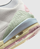 Close-up of a white and pastel Nike sneaker featuring textured leather, mint green and pink accents.
