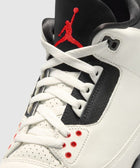 White and black sneaker with red Jumpman logo and red lace eyelets, closeup view
