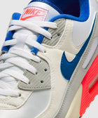 Close-up of Nike Air Max 90 sneaker in white, blue, grey, and neon pink accents