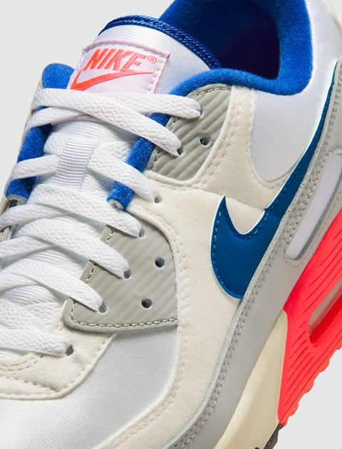 Close-up of Nike Air Max 90 sneaker in white, blue, grey, and neon pink accents