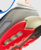 Close-up of an athletic sneaker with a red outsole, air cushion, and grey upper accents