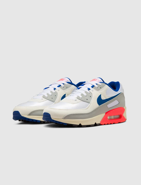 White and grey athletic sneakers with blue swoosh and vibrant red accents on the sole
