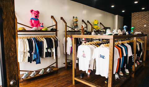 Streetwear clothing store interior with men's t-shirts, sneakers, and colorful bear figures on display.