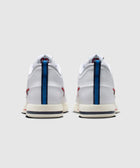 Rear view of white low-top sneakers with blue heel stripe and red accents on a plain background