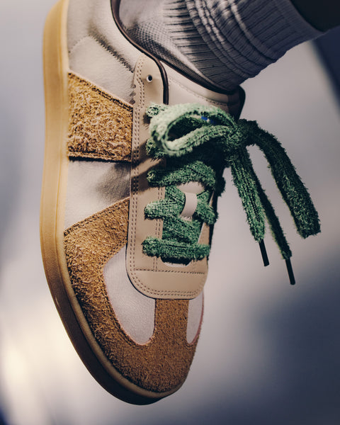 Close-up of a stylish sneaker with tan suede panels and textured green laces