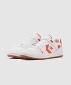 White low top sneakers with orange accents and gum soles on a plain background