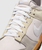 Close-up of Nike low-top sneaker with white and grey suede panels, gum sole, and white laces