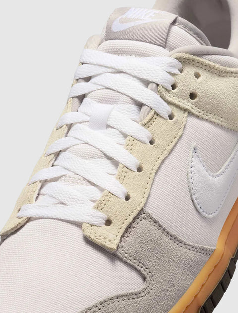 Close-up of Nike low-top sneaker with white and grey suede panels, gum sole, and white laces