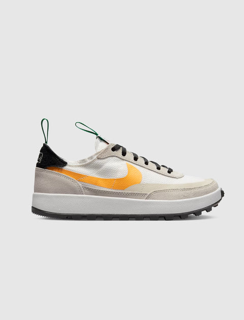White and beige low-top sneaker with orange swoosh, black laces, and green pull tabs