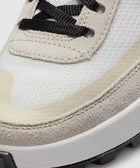 Close-up of a sneaker toe with white mesh, beige suede overlay, and black laces