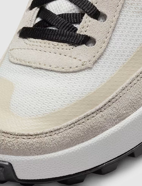 Close-up of a sneaker toe with white mesh, beige suede overlay, and black laces