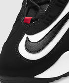 Close-up of black and white sneaker with visible swoosh and red lace loop, streetwear style