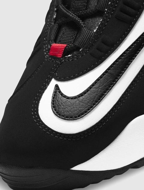 Close-up of black and white sneaker with visible swoosh and red lace loop, streetwear style