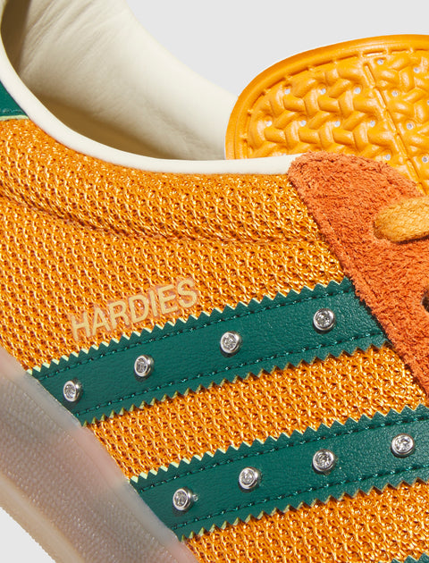 Close-up of orange mesh sneaker with green leather stripes, rhinestone accents, and 'HARDIES' text