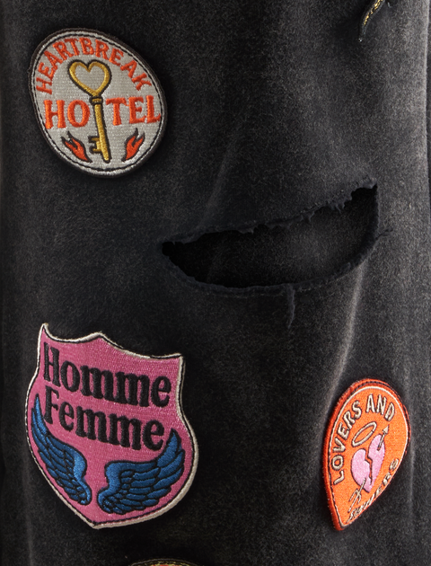 Close-up of black streetwear fabric with embroidered patches and a distressed rip