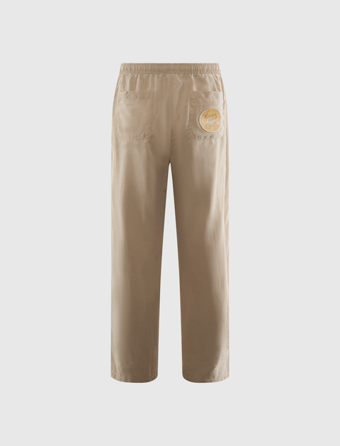 Beige streetwear pants with elastic waistband, back pockets, and yellow patch detail