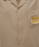 Beige button-up shirt with collar and sun graphic on front chest pocket