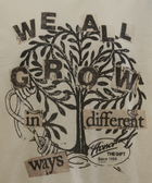 Cream streetwear tee with black graphic tree and 'We all grow in different ways' text print.