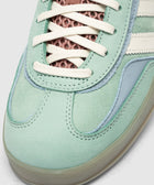 Close-up of mint green suede sneaker with white laces and mesh tongue