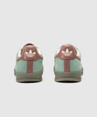 Rear view of green and brown suede sneakers with white logo on heel tab on white background.