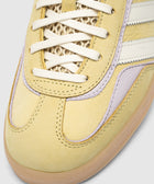 Closeup of yellow suede sneaker with mesh tongue, white laces, and lilac accents