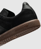 Black suede sneaker with brown textured sole and adidas logo closeup