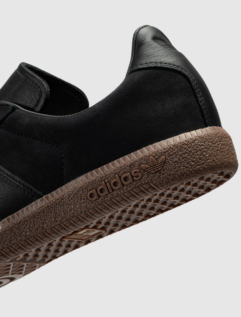 Black suede sneaker with brown textured sole and adidas logo closeup