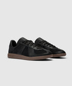 Black low-top sneakers with gum soles and side stitching on a neutral background