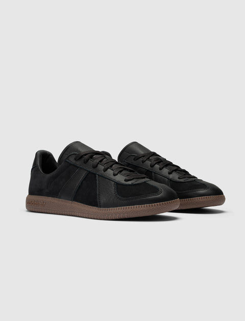 Black low-top sneakers with gum soles and side stitching on a neutral background