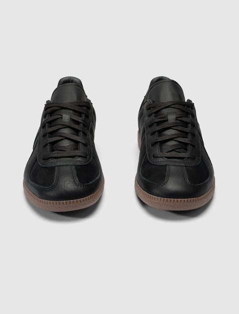Pair of black low-top sneakers with gum soles on a plain background