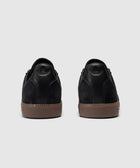 Back view of black low-top sneakers with brown textured rubber soles on gray background