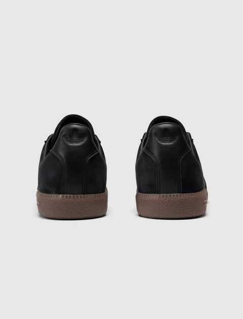Back view of black low-top sneakers with brown textured rubber soles on gray background