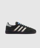 Black suede sneaker with white stripes, grey heel tab, blue label, and gum sole on white background