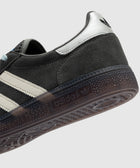 Close-up of grey suede sneaker with white leather stripes, gum sole, and black logo heel tab