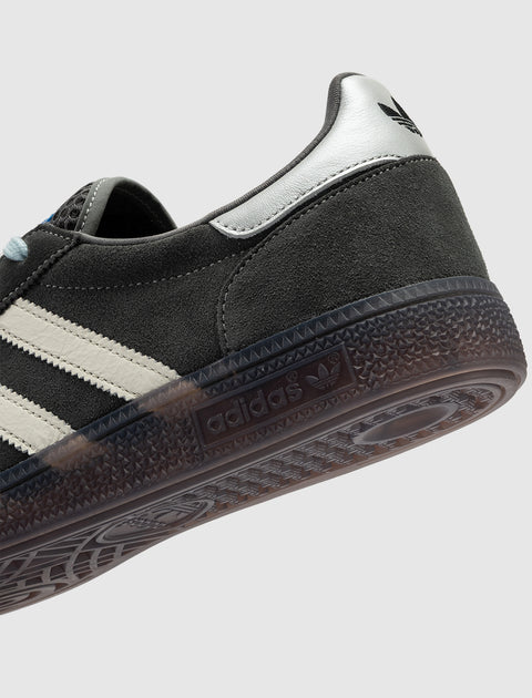 Close-up of grey suede sneaker with white leather stripes, gum sole, and black logo heel tab