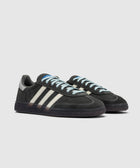 Black suede low-top sneakers with cream stripes and light blue laces on a grey background