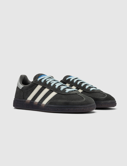 Black suede low-top sneakers with cream stripes and light blue laces on a grey background