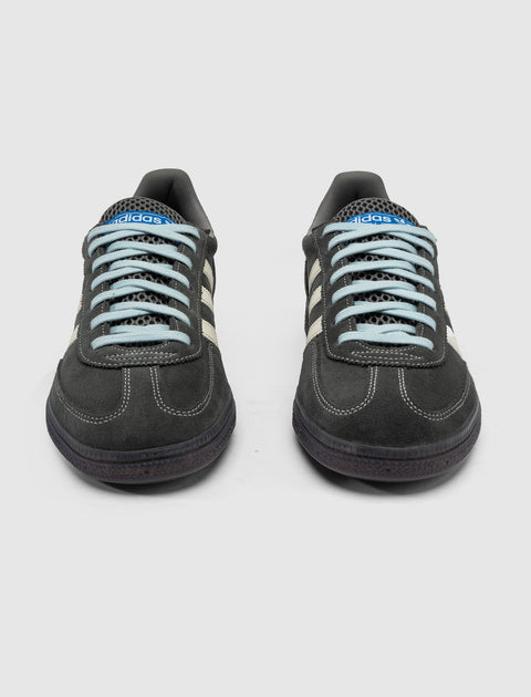 Front view of grey suede sneakers with cream stripes and blue laces, on white background.