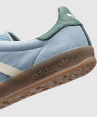 Light blue suede sneaker with green heel tab, gum sole, and white side stripes