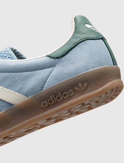 Light blue suede sneaker with green heel tab, gum sole, and white side stripes