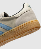 Closeup of grey suede sneaker with blue stripes, gum sole, and adidas logo detail