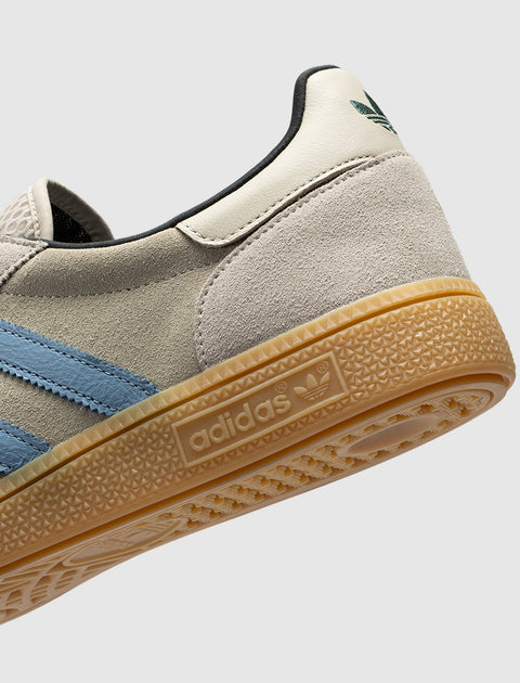 Closeup of grey suede sneaker with blue stripes, gum sole, and adidas logo detail