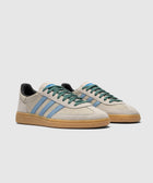 Beige suede sneakers with light blue stripes, gum sole, and green laces on white background.