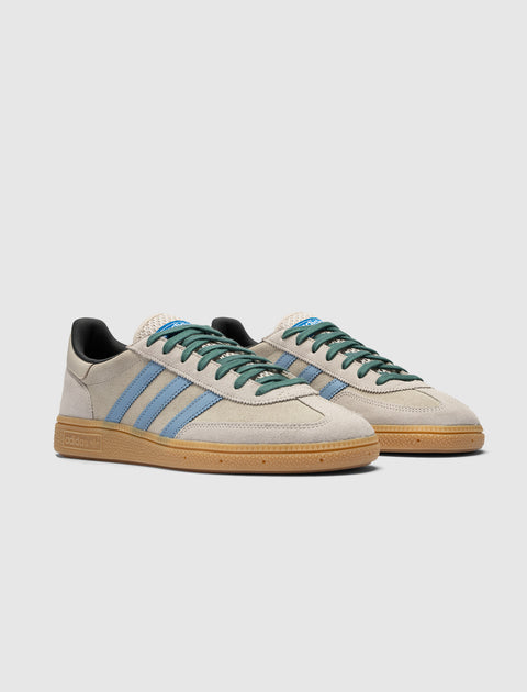 Beige suede sneakers with light blue stripes, gum sole, and green laces on white background.