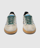Beige suede low-top sneakers with green laces, blue stripes, and gum soles on white background.