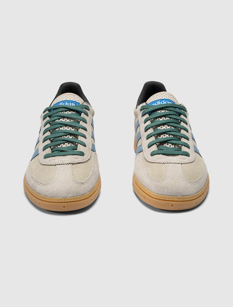 Beige suede low-top sneakers with green laces, blue stripes, and gum soles on white background.